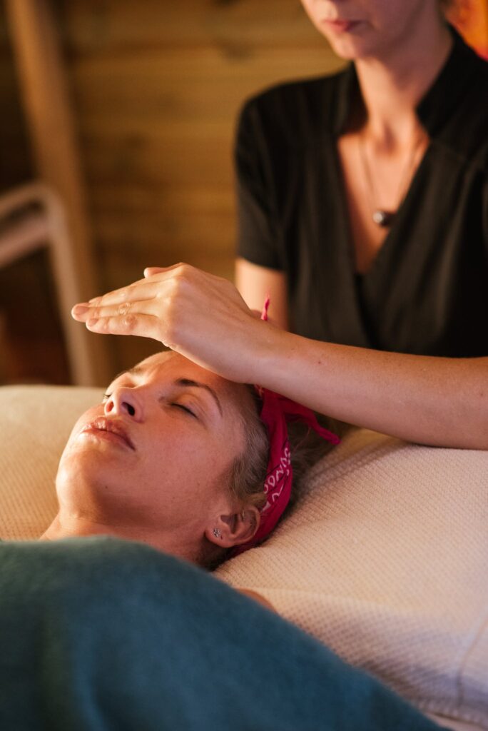 Relaxed woman with closed eyes lying under blanket while getting reiki therapy treatment from unrecognizable therapist in cozy salon with blurred background